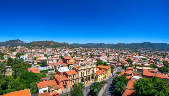 Aerial view of San Miguel de Allende featuring colourful colonial buildings, cobblestone streets, and green hills under a clear blue sky.