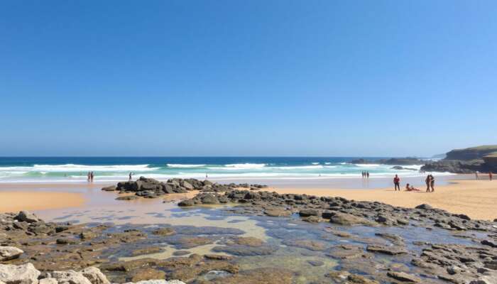 A sunlit beach with clear waves, golden sands for sunbathing, rocky outcrops for exploration, accessible ramps, and diverse individuals enjoying the day under a blue sky.